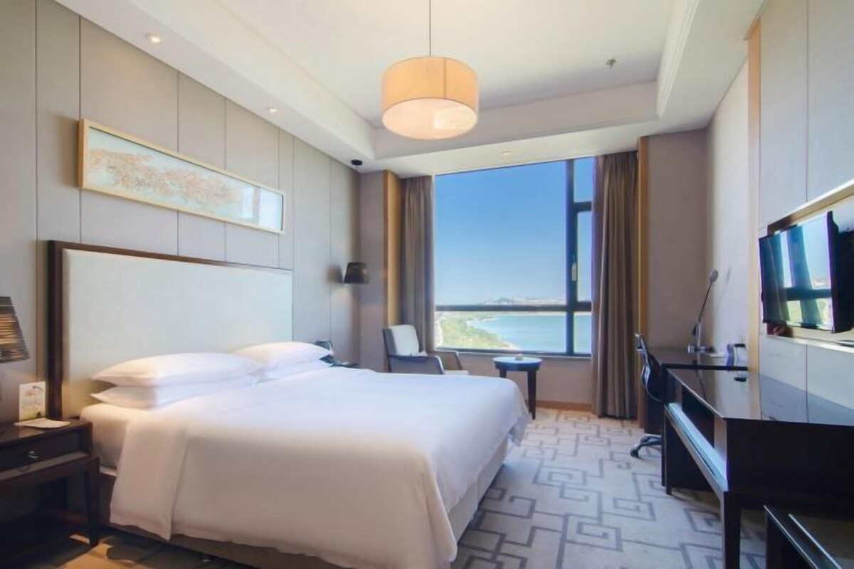 Hotelkamer met een groot bed, een bureau, een stoel, een televisie en een raam met uitzicht op zee.