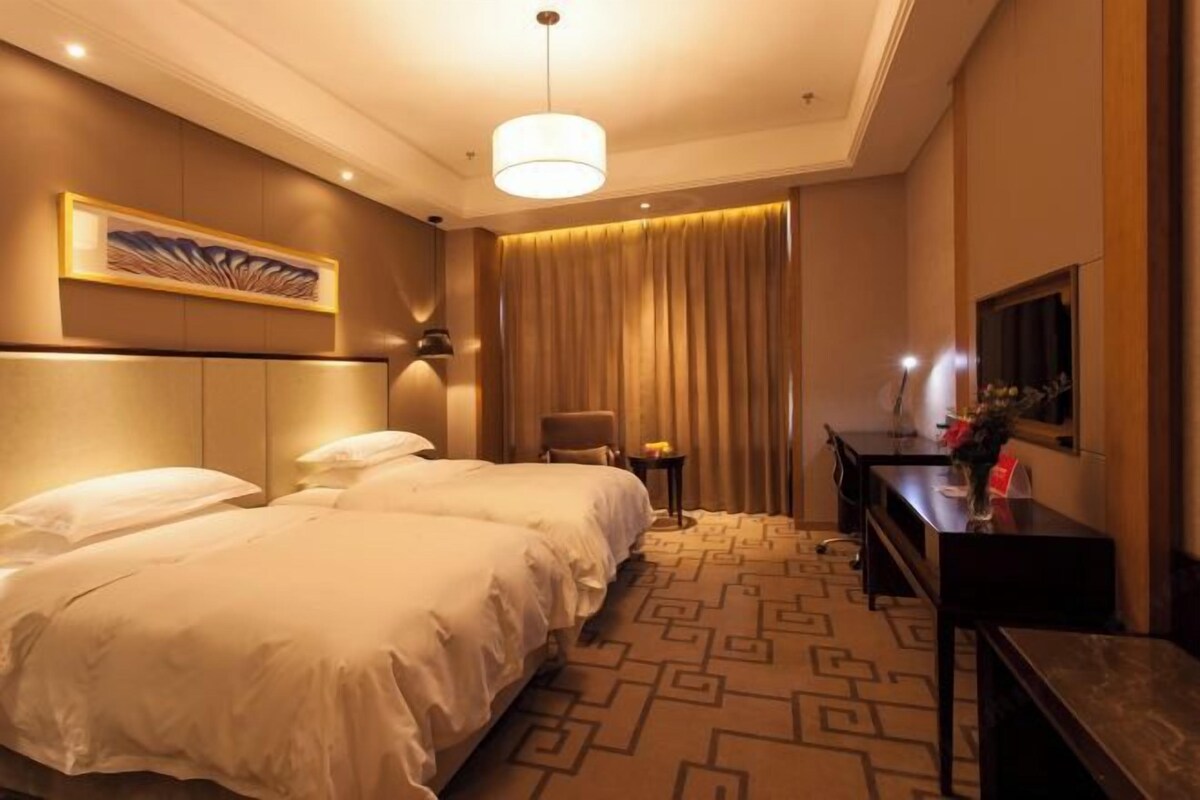 Habitación de hotel con dos camas, un escritorio, una silla, un televisor y un cuadro en la pared.
