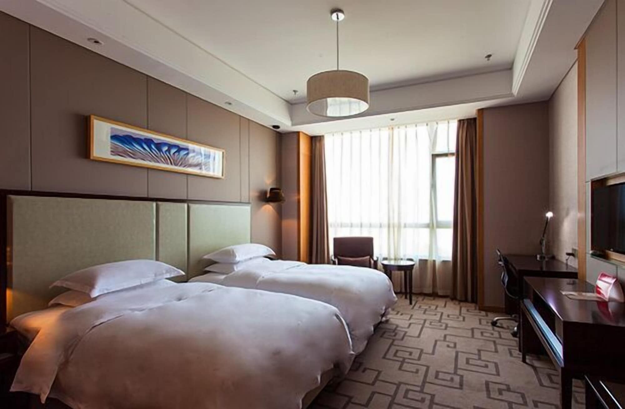 A hotel room with two beds, a desk, a chair, a television, and a large window with curtains.