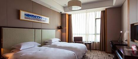 Quarto de hotel com duas camas, uma escrivaninha, uma cadeira, televisão e uma janela grande com cortinas.