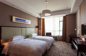 Habitación de hotel con dos camas, un escritorio, una silla, un televisor y un ventanal con cortinas.