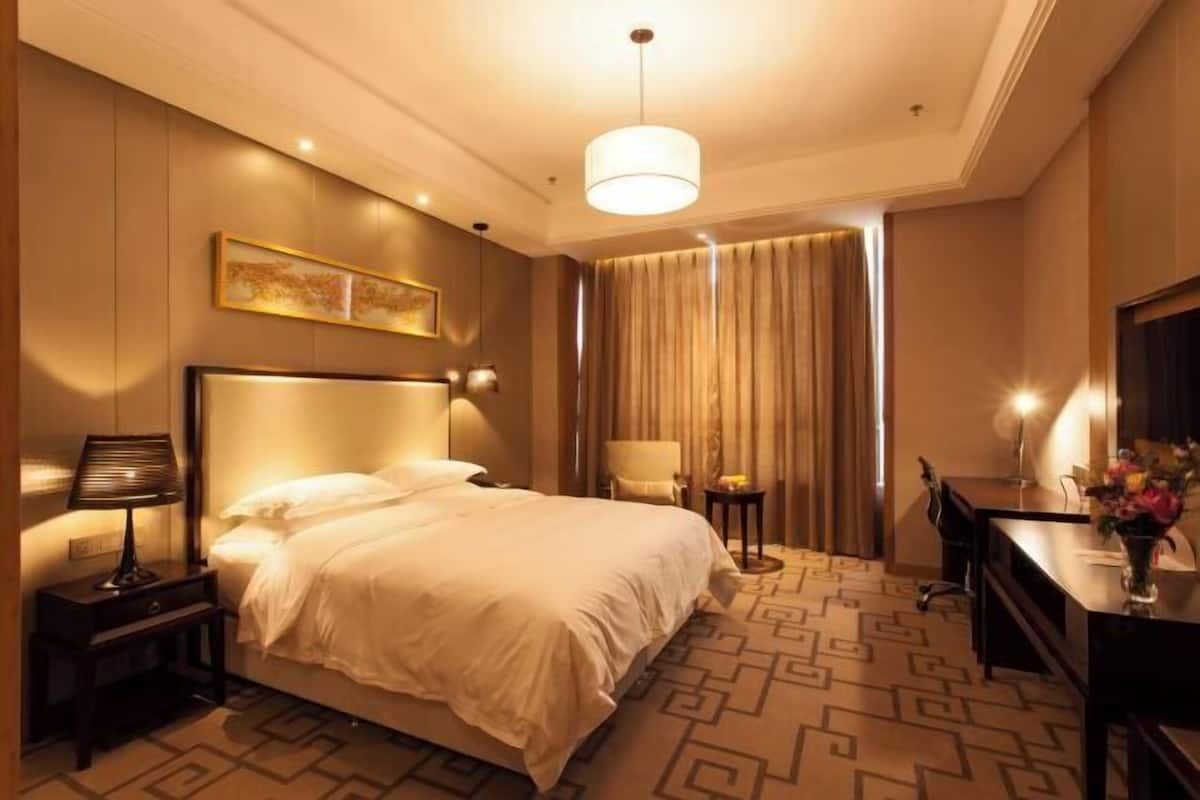 A hotel room with a large bed, a desk, a chair, a lamp, a mirror, and a painting on the wall.