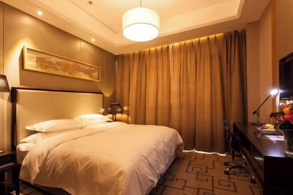 A hotel room with a large bed, a desk with a lamp, a television, and a painting on the wall.