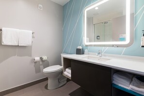 A modern bathroom with a toilet, sink, and mirror, featuring a towel rack and a visible toilet paper holder. - avid hotel Summerville by IHG (Summerville)