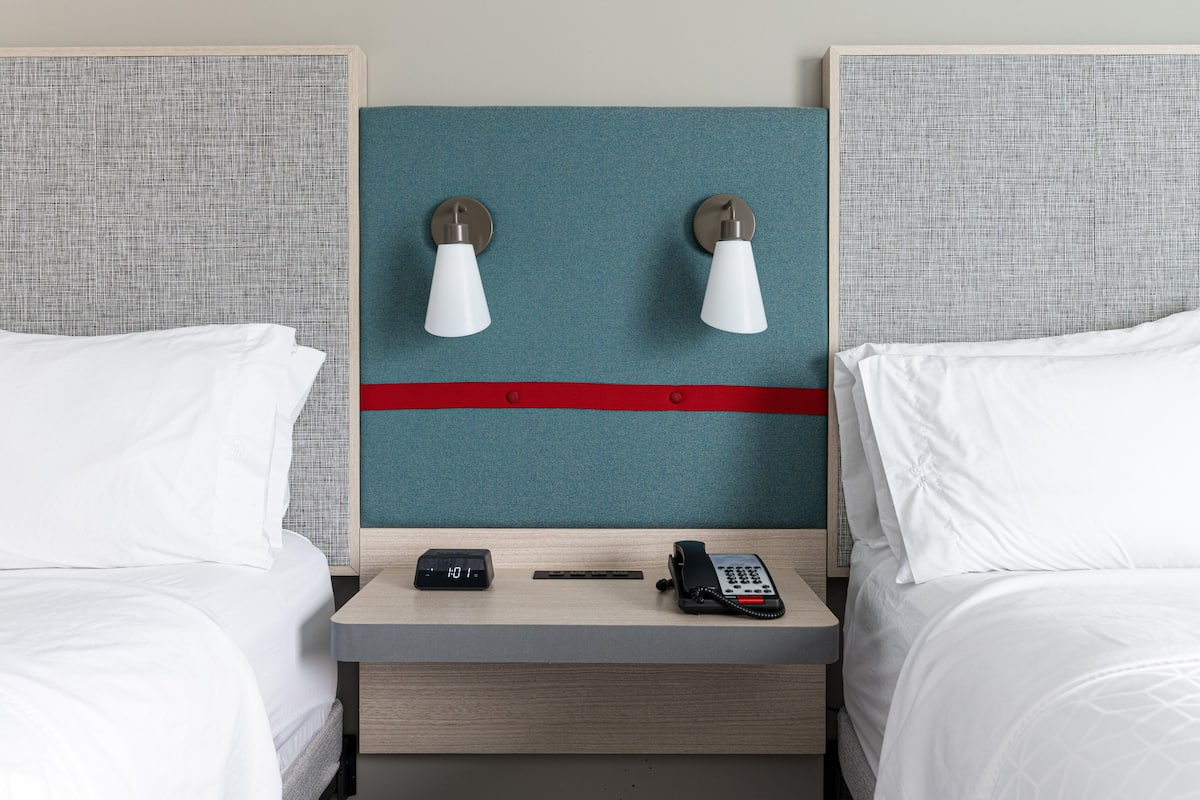 Une chambre d’hôtel avec deux lits, une table de chevet, une horloge et un téléphone.