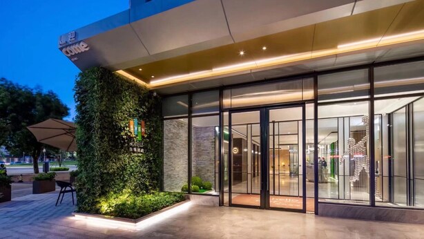 L’entrée d’un hôtel avec une façade en verre, un jardin vertical verdoyant et un design moderne.
