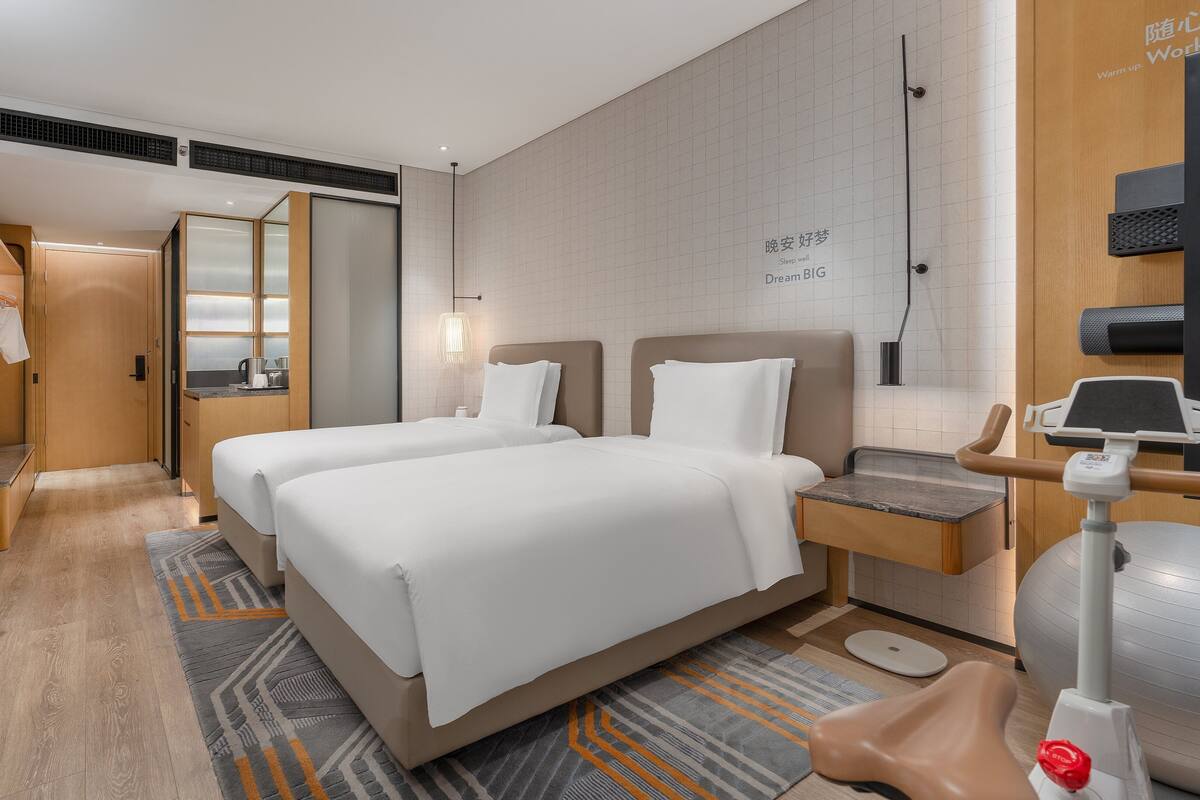 A hotel room with two beds, a desk, a treadmill, and a massage chair.