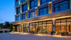 Un hôtel moderne doté d’une façade en verre, d’un espace extérieur aménagé et d’une entrée bien éclairée.