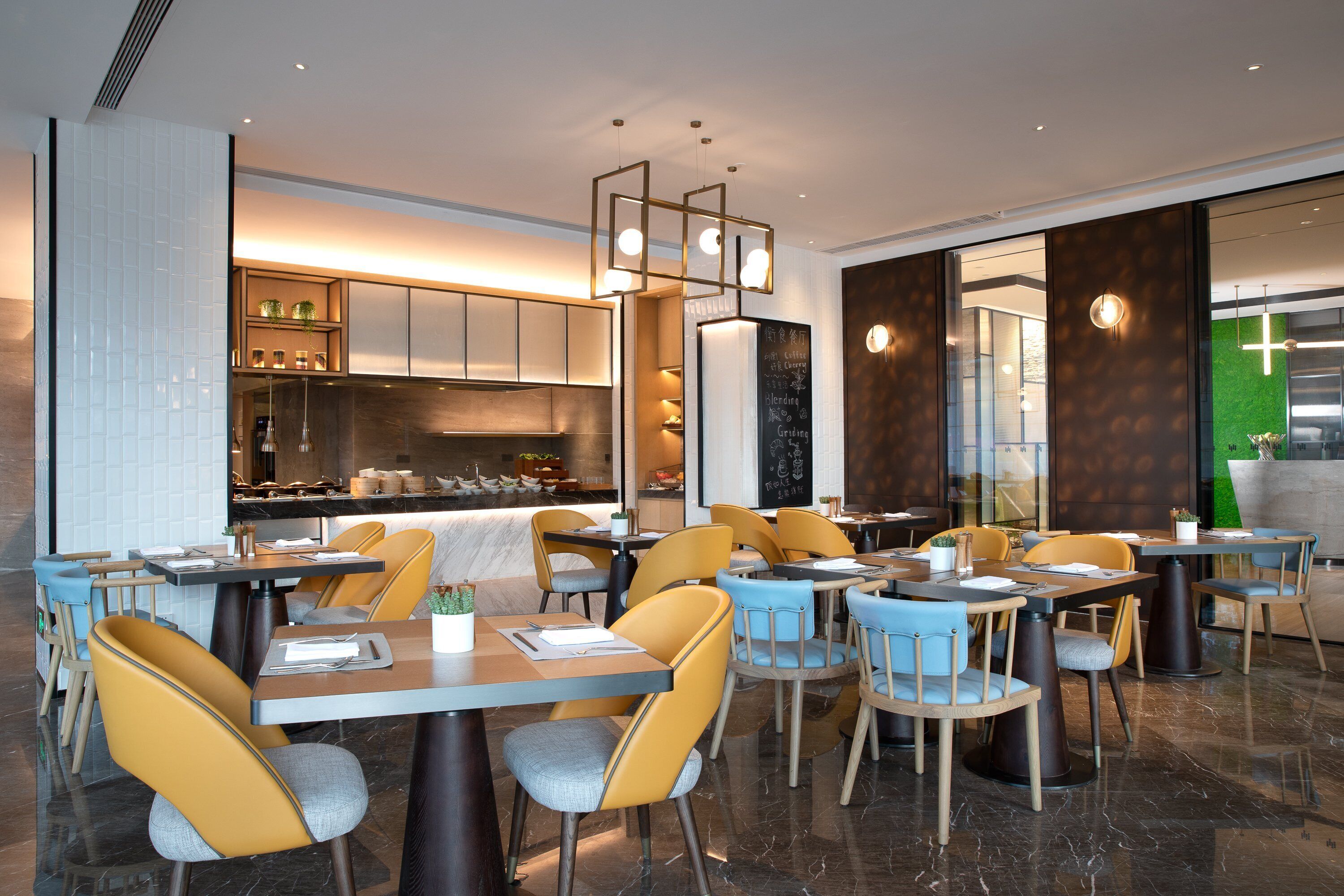 Un restaurante moderno con zona de bar, asientos con sillas amarillas y azules, y una cocina visible al fondo.
