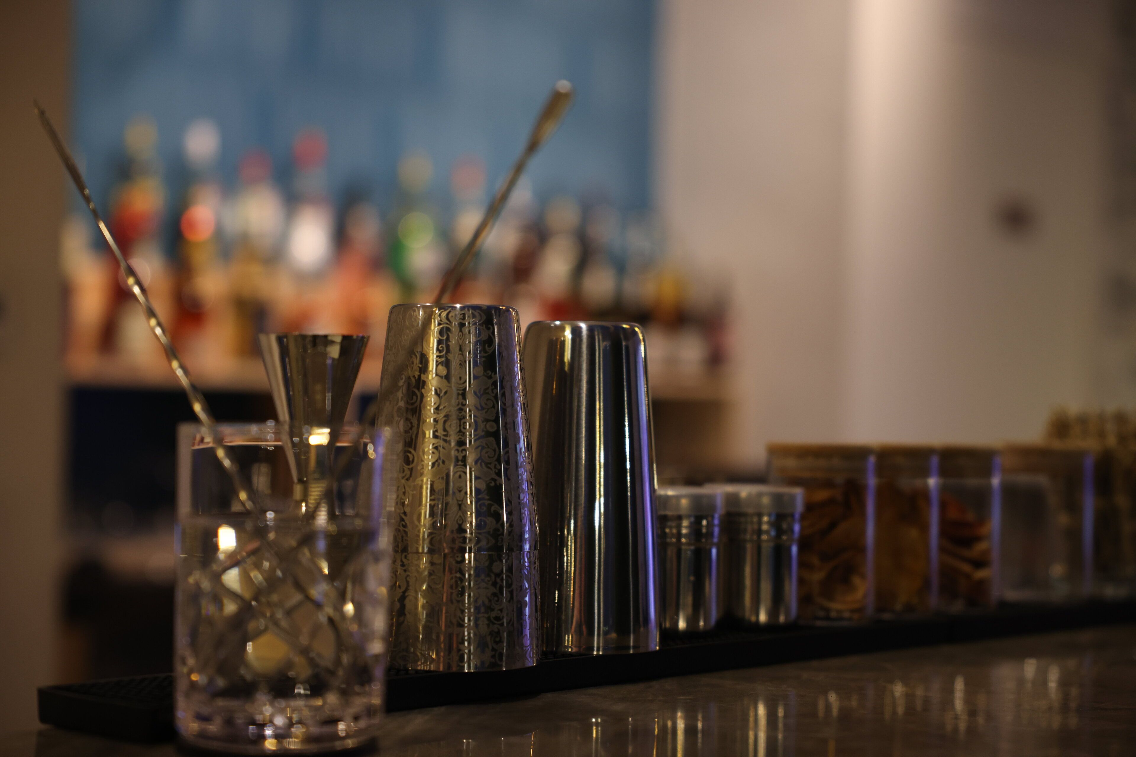 Zona de bar con distintos vasos y utensilios, incluyendo un vaso con pajita y un recipiente metálico.