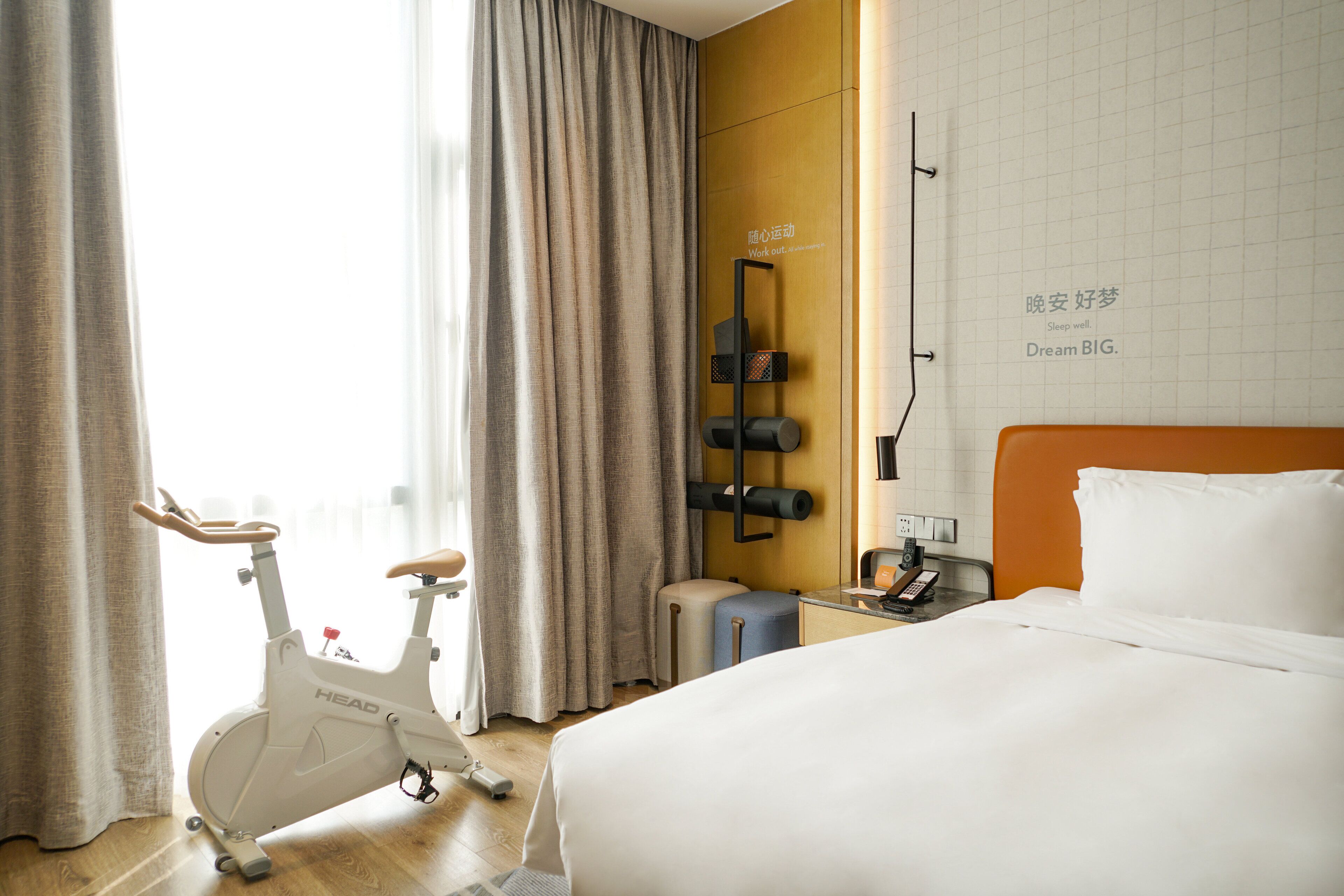 Quarto de hotel com cama, bicicleta ergométrica e TV fixada na parede.