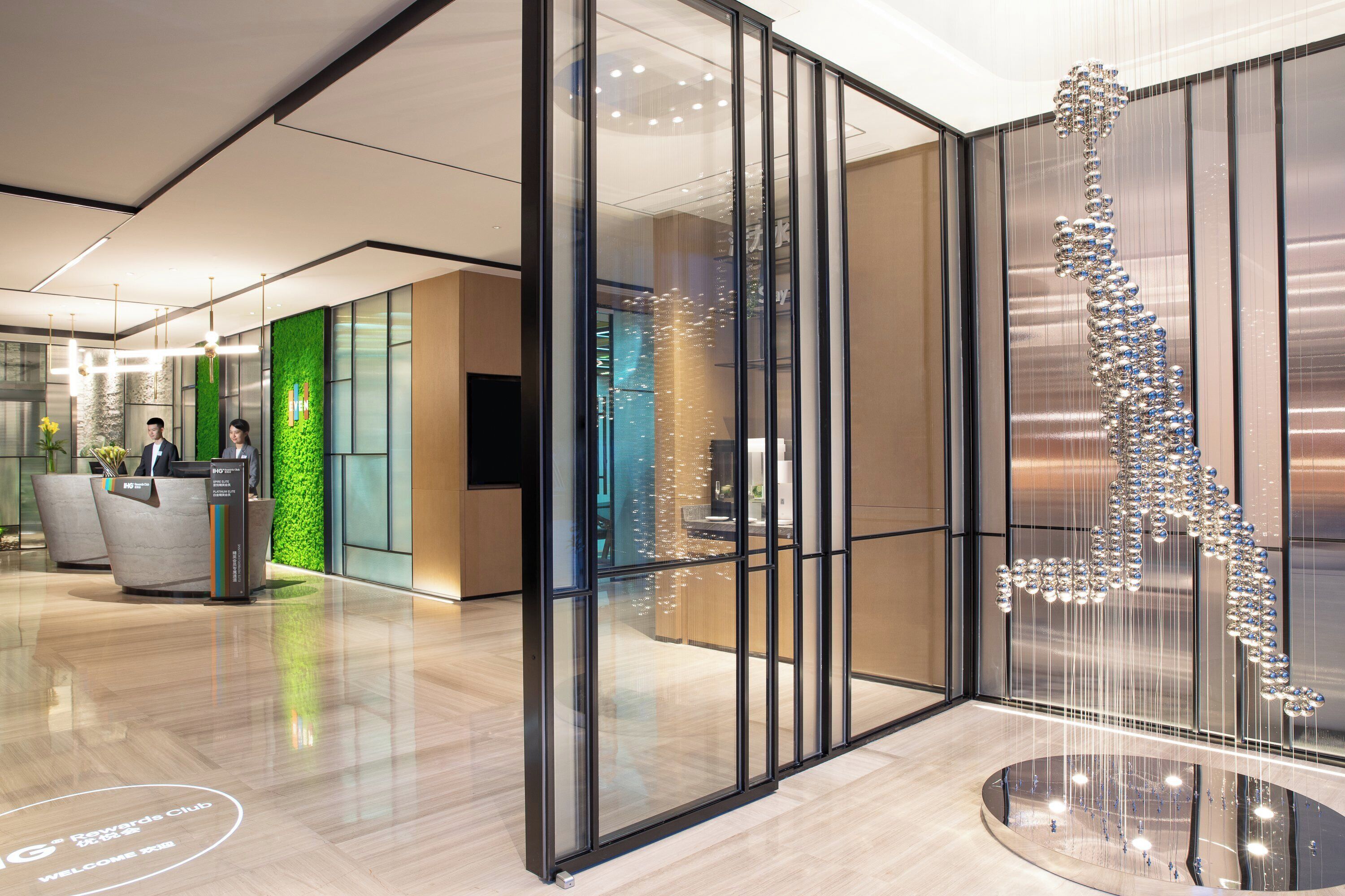 A modern reception area with a glass partition, a reception desk, and a decorative hanging sculpture.