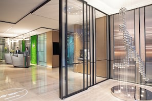 A modern reception area with a glass partition, a reception desk, and a decorative hanging sculpture. - EVEN Hotel Shenzhen Nanshan by IHG (Shenzhen)