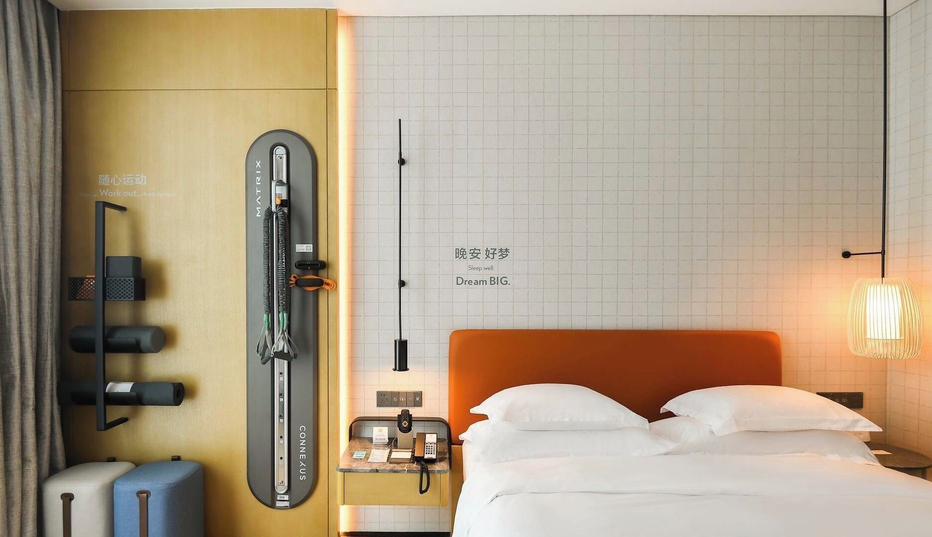 Een hotelkamer met een bed, een massagestoel, een kleine tafel met een telefoon en een aan de muur bevestigd trainingsapparaat.