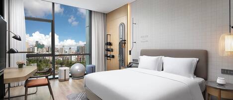 A modern hotel room with a large bed, a desk, and a view of the city skyline through floor-to-ceiling windows.