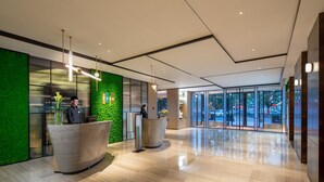 Un espace d’accueil moderne agrémenté d’un mur végétal, de deux comptoirs d’accueil et d’une entrée en verre donnant sur l’extérieur.