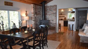 A dining area with a brick fireplace, wooden dining table, and chairs. - Beautiful Ocean View Home on the Majestic Oregon Coast The Blue Pelican (Brookings)
