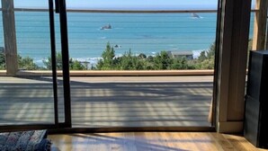 A room with a large sliding glass door leading to a balcony with a view of the ocean and a distant shoreline. - Beautiful Ocean View Home on the Majestic Oregon Coast The Blue Pelican (Brookings)