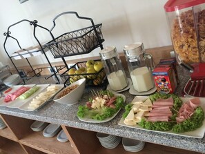 A buffet table with various food items including fruits, cheeses, and meats, along with condiments and beverages. - Hit Hoteles Aeropuerto Puebla (Huejotzingo)