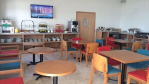 A dining area with round tables and chairs, a coffee machine, and a television mounted on the wall. - Hit Hoteles Aeropuerto Puebla (Huejotzingo)