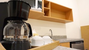 A coffee maker, a tray with cups, a sink, and a dishwashing machine in a kitchen. - Hit Hoteles Aeropuerto Puebla (Huejotzingo)