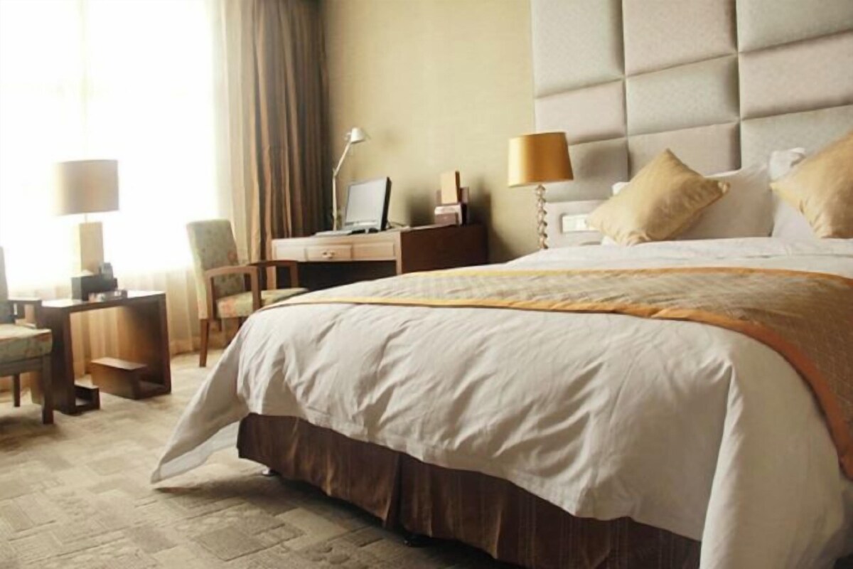 A hotel room with a large bed, a desk with a computer, a chair, and a lamp.