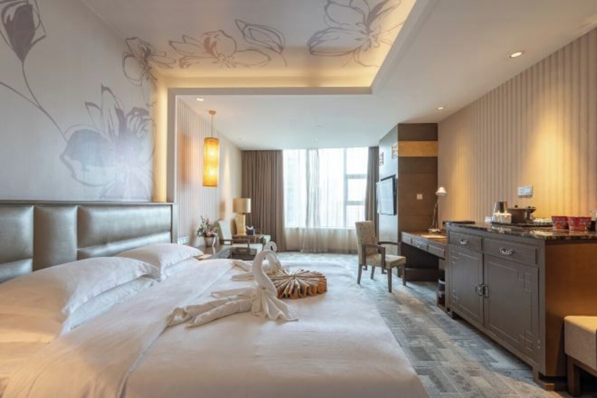 A hotel room with a large bed, a desk, a wardrobe, and a dining area.