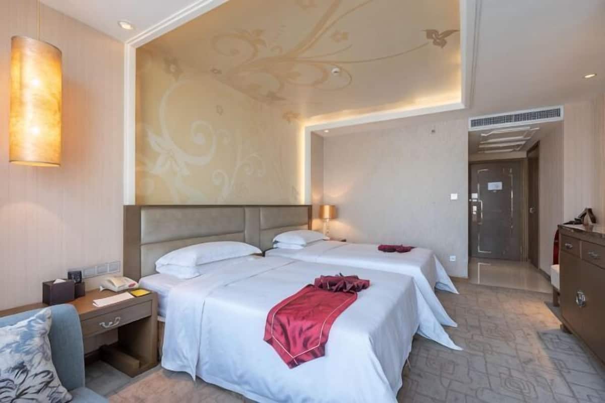 A hotel room with two beds, a desk with a telephone, a wardrobe, and a decorative wall.