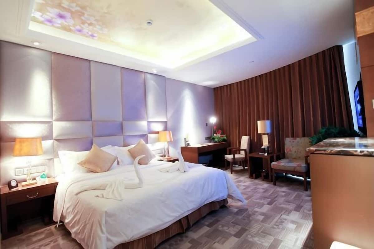 A hotel room with a large bed, bedside tables, a desk, a chair, and a television.