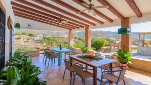 Un patio al aire libre con una mesa, sillas, un ventilador de techo y vistas del paisaje circundante.