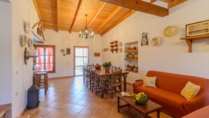 Un espacio habitable amplio con techo de madera, una mesa de comedor con sillas, un sofá y varios objetos decorativos en las paredes.