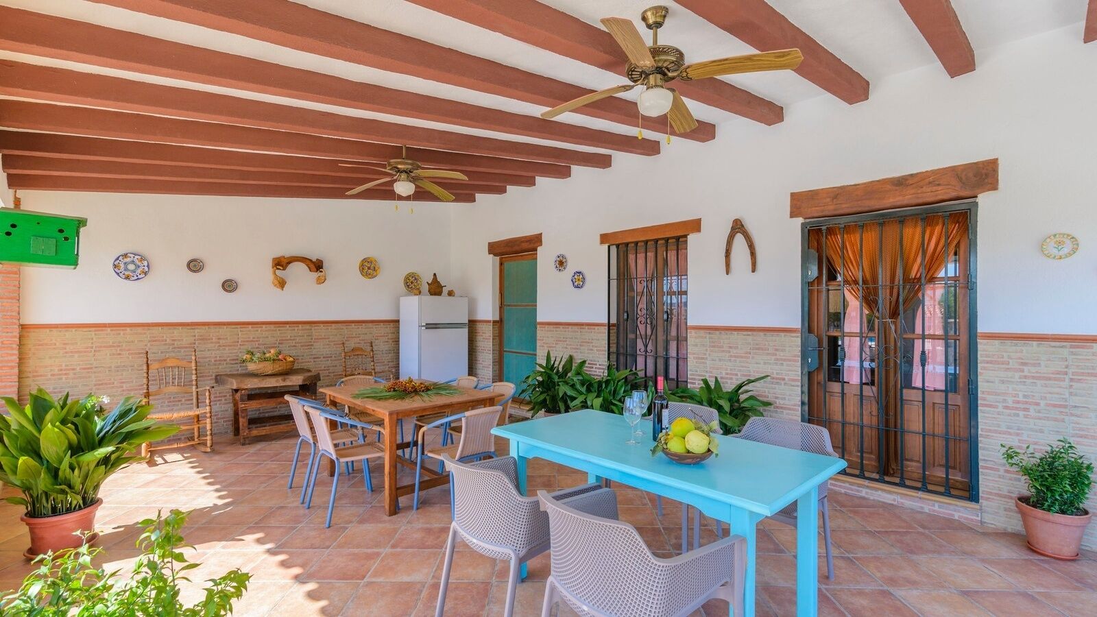 A patio with a table and chairs, a ceiling fan, and potted plants.