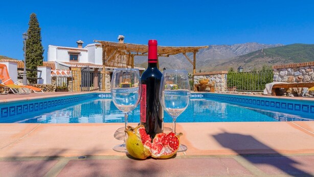 Escena junto a la piscina con una botella de vino, dos copas y una granada.
