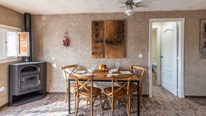 A dining area with a table set for four, surrounded by wooden chairs. A black wood stove is visible to the left, and a ceiling fan is above the table. - El Balcón del Olivar Villanueva de Algaidas by Ruralidays (Málaga)