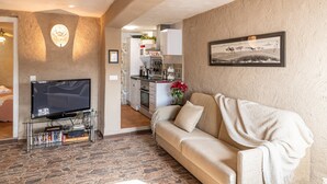 A living room with a television, a sofa, and a coffee table. There is a kitchen in the background. - El Balcón del Olivar Villanueva de Algaidas by Ruralidays (Málaga)