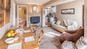 A dining area with a wooden table set for four, a sofa, and a television in the background. - El Balcón del Olivar Villanueva de Algaidas by Ruralidays (Málaga)