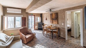 A cozy room with a stone floor, a fireplace, a dining table with chairs, a sofa, and a ceiling fan. - El Balcón del Olivar Villanueva de Algaidas by Ruralidays (Málaga)