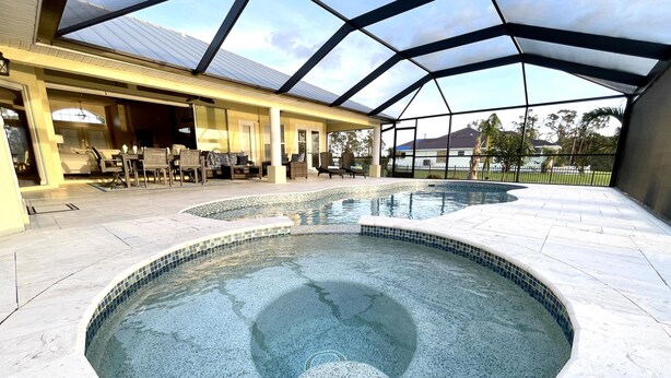Une piscine entourée de parois en verre, un patio couvert aménagé avec du mobilier d’extérieur, et une vue sur le paysage environnant.