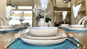 Une table à manger dressée avec des bols blancs à texture, de la vaisselle transparente et des sets de table bleus.