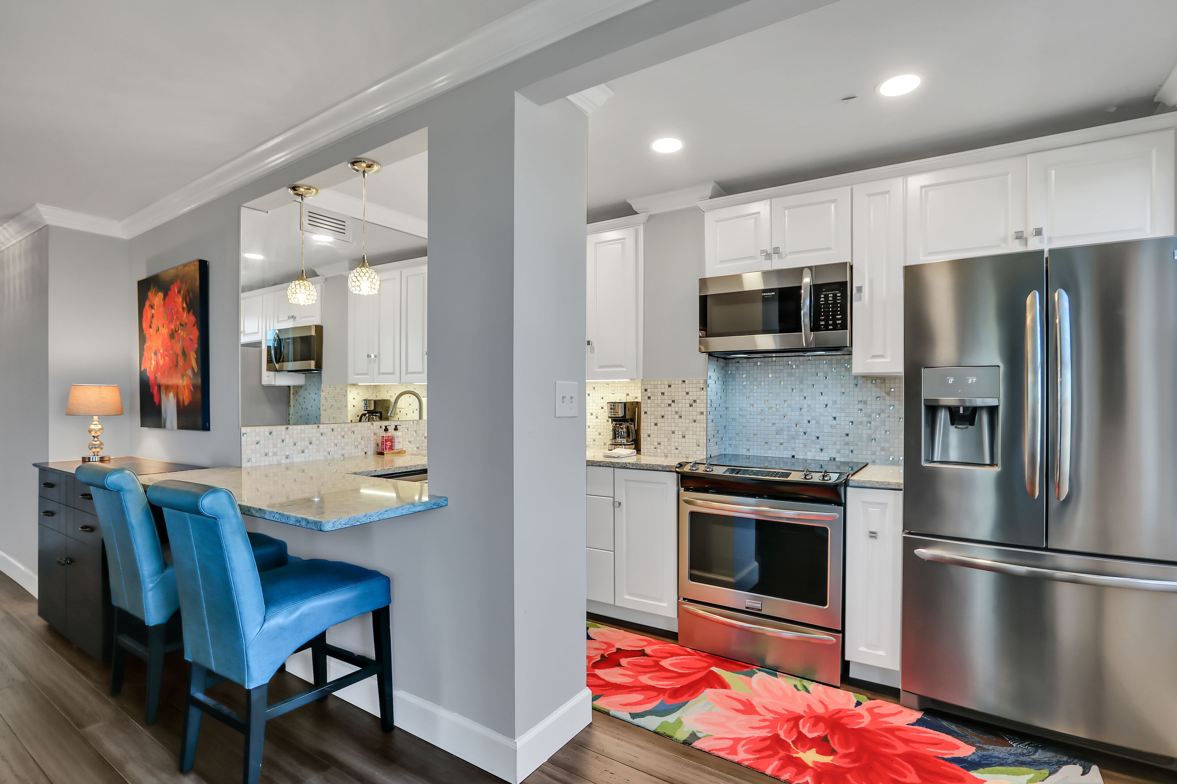 A modern kitchen with white cabinets, stainless steel appliances, and a blue bar area with matching chairs.