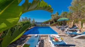 Un espace piscine avec des chaises longues et une table sur laquelle se trouvent une pastèque et des boissons.