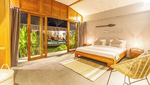 Un dormitorio con un amplio ventanal corredizo que da a una zona de piscina, una cama con almohadas estampadas y una silla de mimbre.