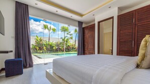 A modern bedroom with a large bed, a view of a swimming pool, and a balcony with tropical plants.
