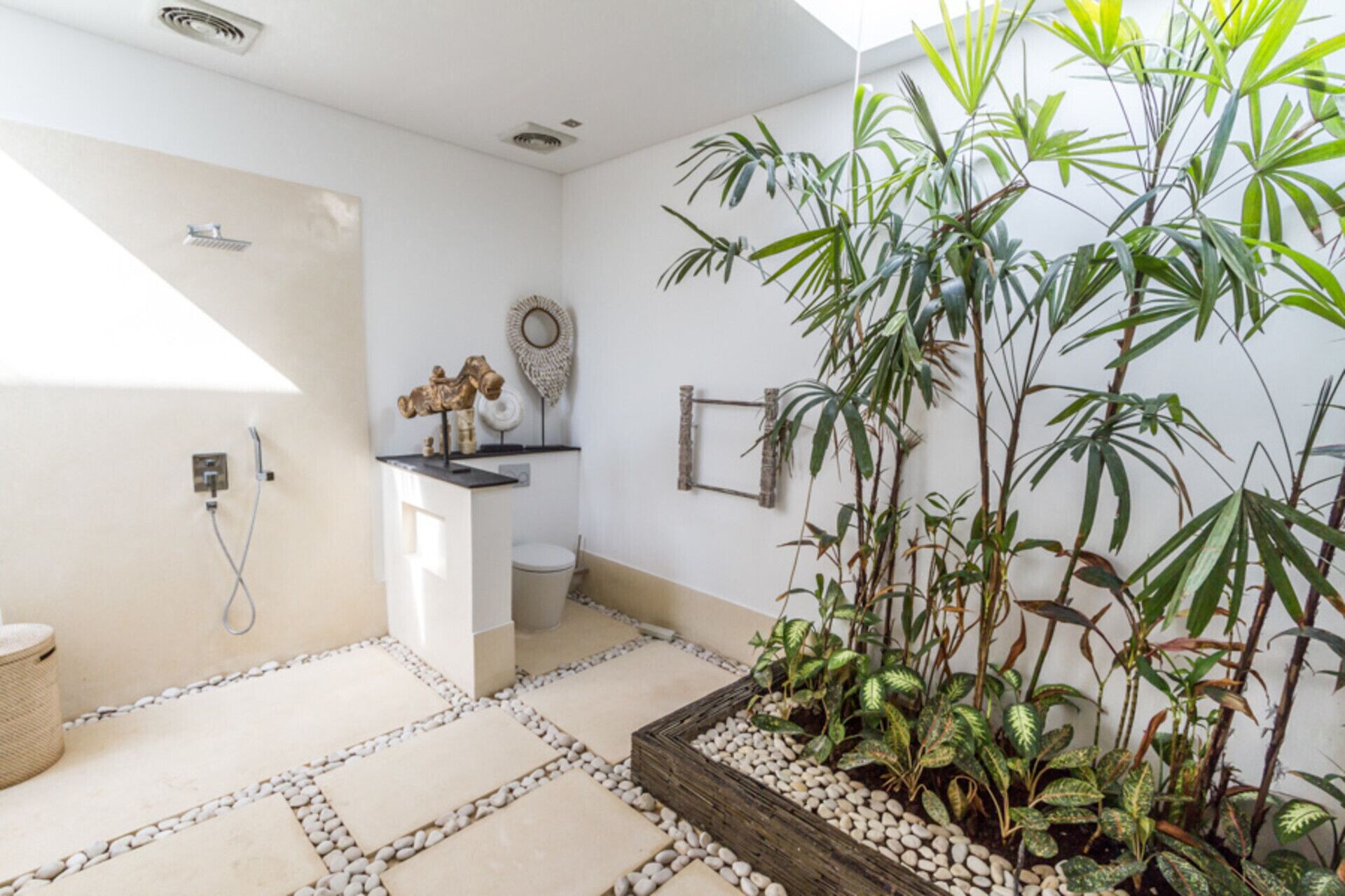 Un baño con ducha, inodoro y lavamanos. Hay plantas decorativas y un espejo en la pared.