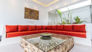A modern living room with a red sofa, a glass coffee table with a natural stone base, and a decorative wall piece. - 5 Star Private Villa Holiday in Seminyak at an Unbeatable Rate, Bali Villa 1158 (Bali)