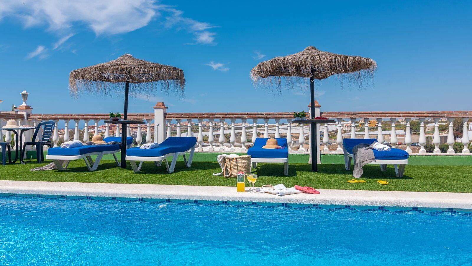 A poolside area with lounge chairs and umbrellas, a clear blue pool, and a view of buildings in the background.