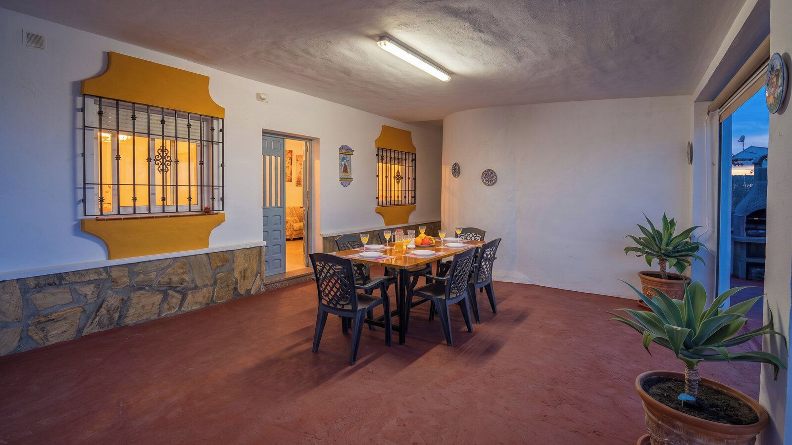 A dining area with a table set for four, surrounded by chairs, with a stone wall and a window with bars on one side.