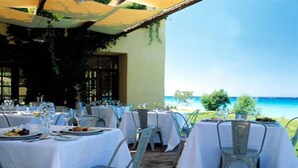 An outdoor dining area with tables set for a meal, overlooking a scenic view of the sea. - Miramare Park (Rhodes)