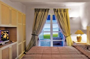 Un dormitorio con cama, televisión en un estante, ventana con cortinas y vistas al exterior.