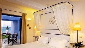 A hotel room with a bed, a clock on the wall, a balcony with a view, and two lamps. - Miramare Park (Rhodes)